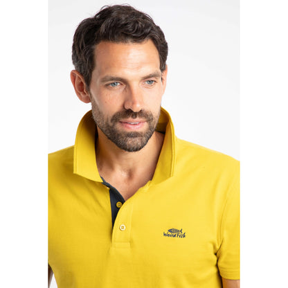 Man wearing a Weird Fish Miles Antique Moss yellow polo shirt with a logo on a white background