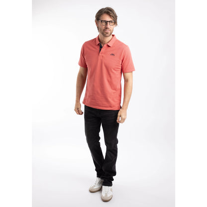 Man wearing a Weird Fish short sleeve Miles polo shirt in Nantucket coral with black trousers.