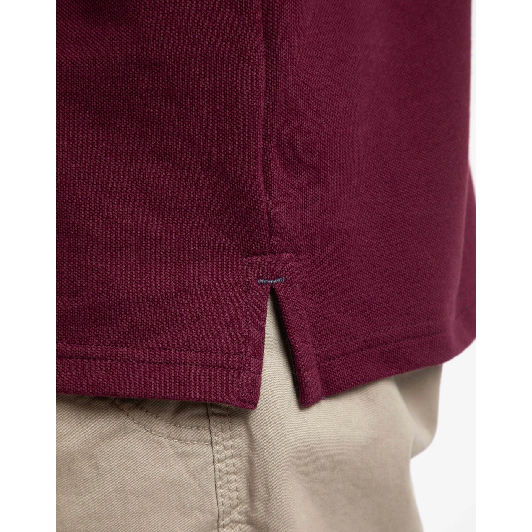 Close-up of a Weird Fish men's Miles maroon polo shirt side slit with beige pants in the background