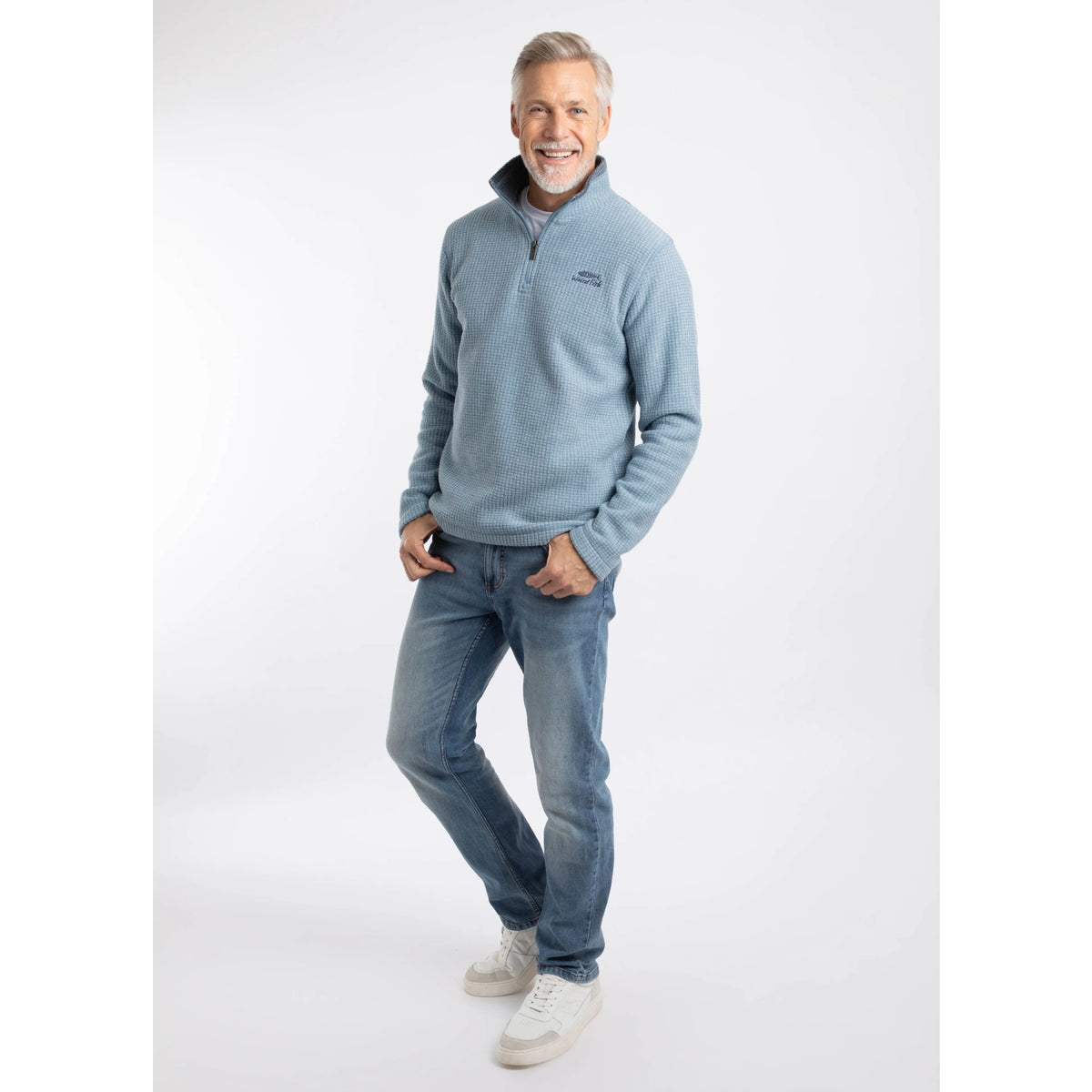 Man wearing a Weird Fish Newark 1/4 zip grid fleece in light blue, with blue jeans and trainers