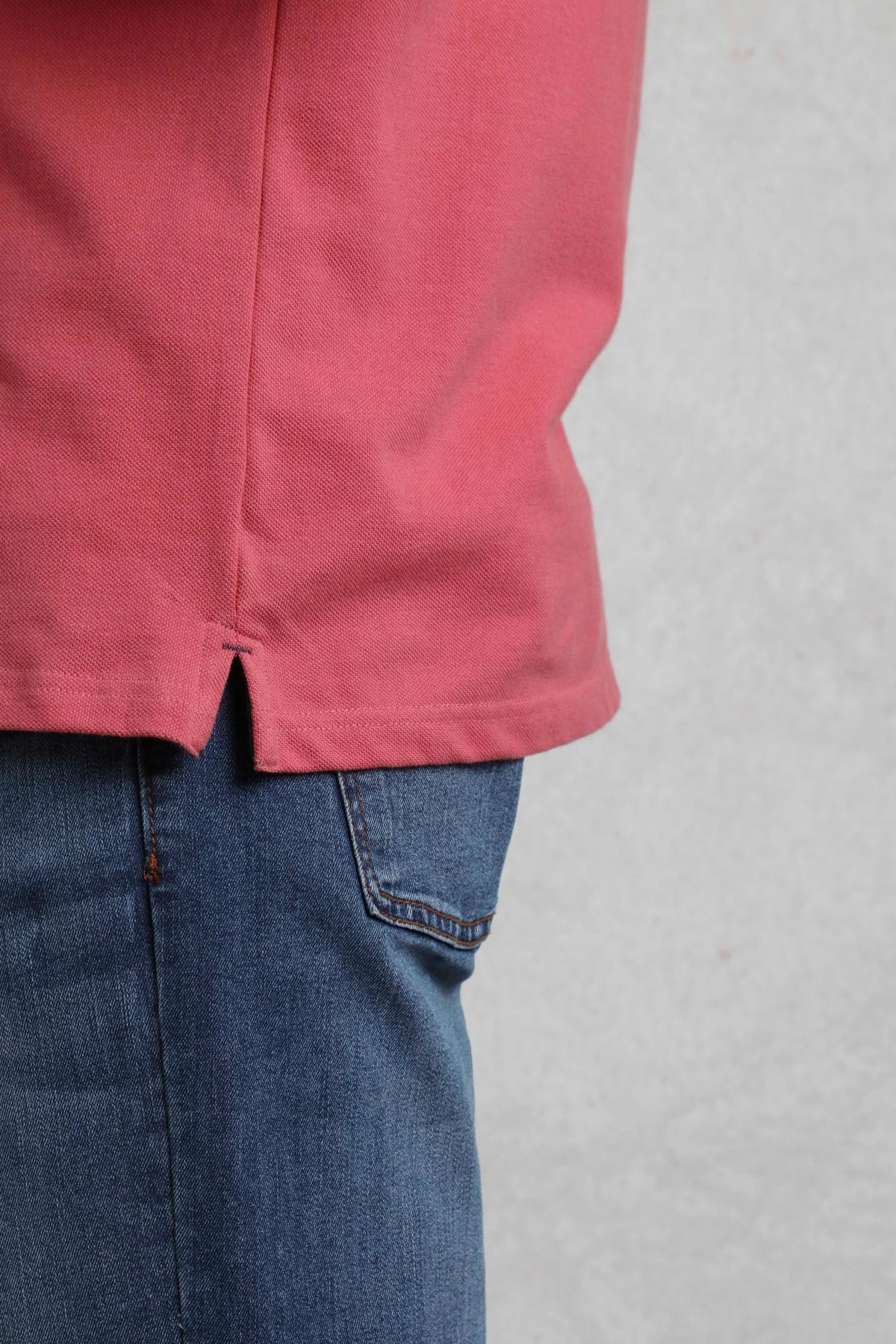 Close-up of Weird Fish mens polo shirt dark pink hem paired with blue denim jeans