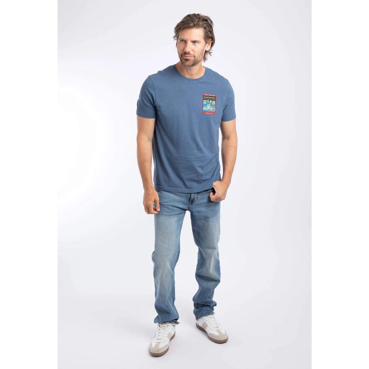 A man wearing a short sleeve t-shirt in Ensign Blue, featuring a small Shawshark Redemption parody print of The Shawshank Redemption film poster on one side of the chest with jeans.