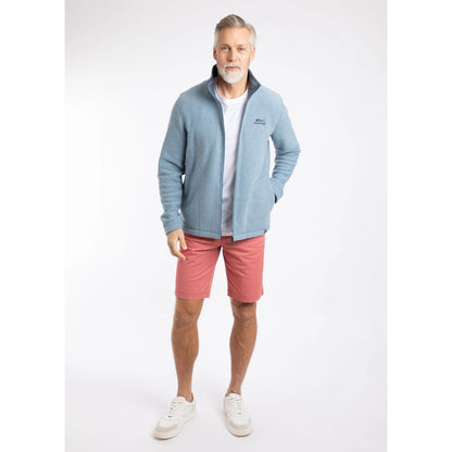 Front view of a man wearing a Weird Fish full zip Shires grid textured fleece in Light Blue unzipped with a white t-shirt, contrasting navy neckline and small chest logo with pink shorts