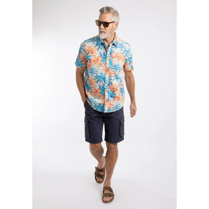 Man wearing a Weird Fish short sleeve Faraway shirt in Paprika orange and blue with a tropical palm tree pattern, with navy shorts and brown sandals