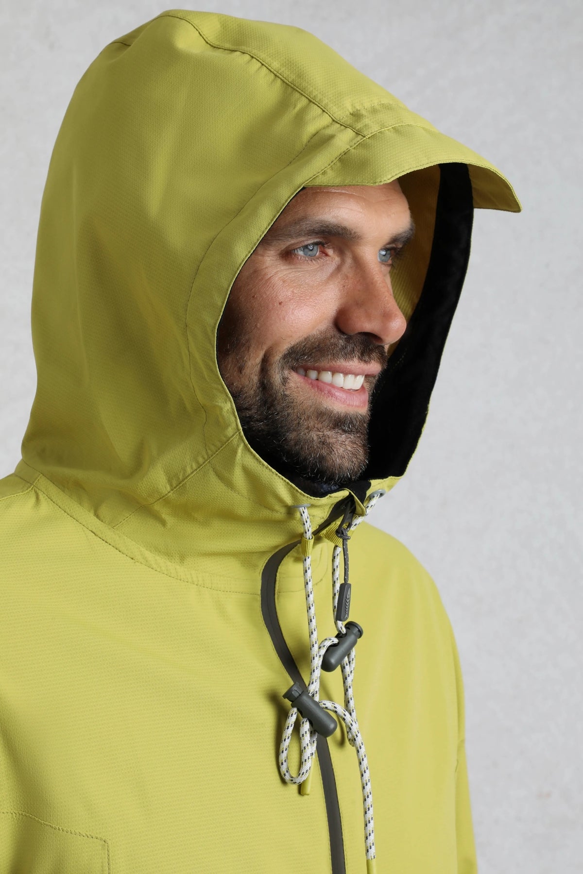 Weird Fish mens waterproof jacket tarragon with hood and drawstring detail on a smiling man