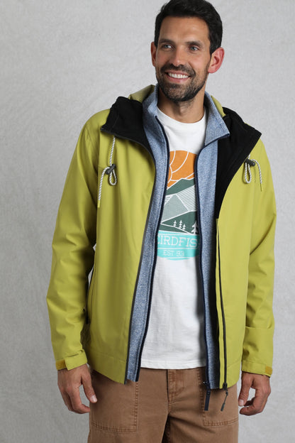 Weird Fish mens waterproof jacket tarragon in green worn by man with brown pants and graphic tee