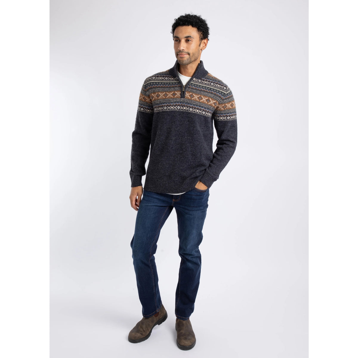 A mman wearing a Weird Fish 1/4 zip Larner knitted jumper in Midnight Navy with a Fair Isle pattern across the chest and shoulders with blue jeans and brown boots.
