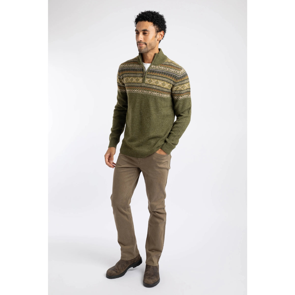 A man wearing a Weird Fish 1/4 zip Larner knitted jumper in Winter Green with a Fair Isle pattern across the chest and shoulders with brown trousers and boots.