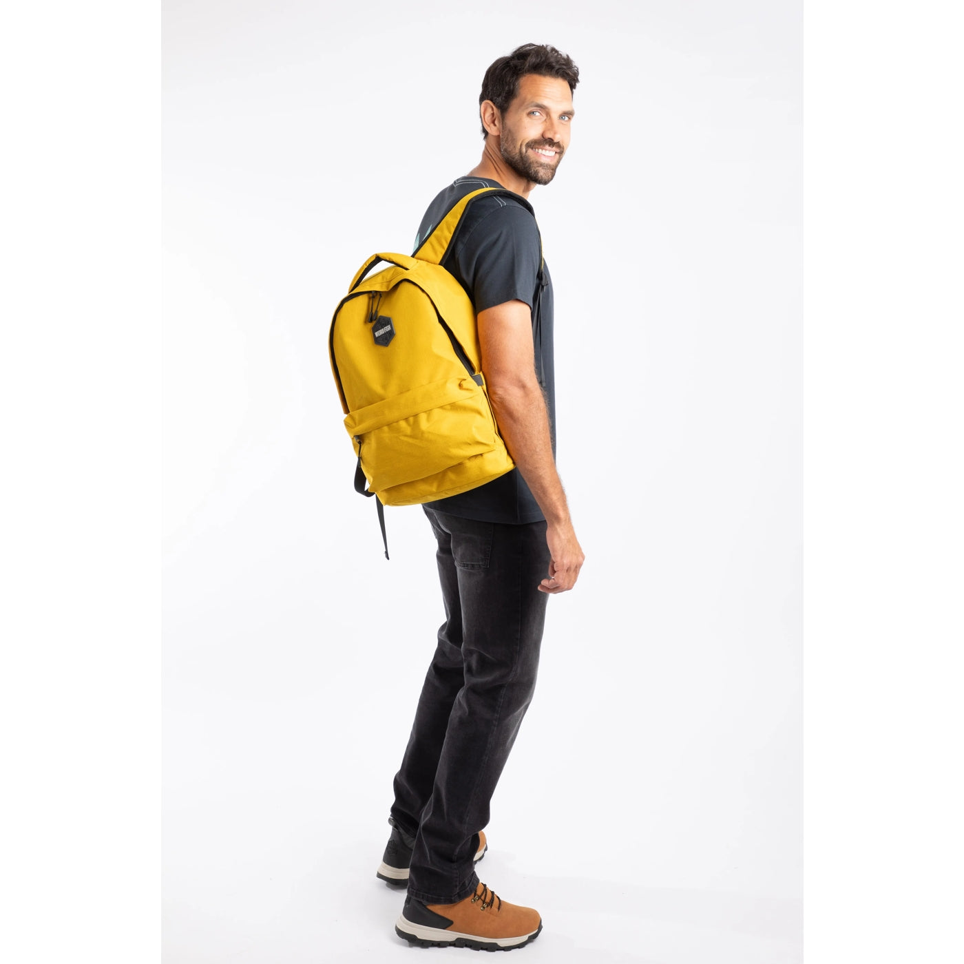 Side view of a man carrying a Weird Fish Nevis yellow backpack.