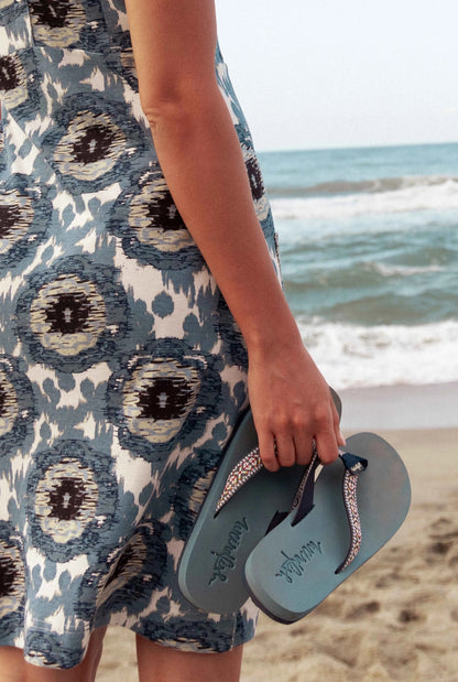 Woman holding Weird Fish womens Adila flip flops by the ocean beach in a patterned dress