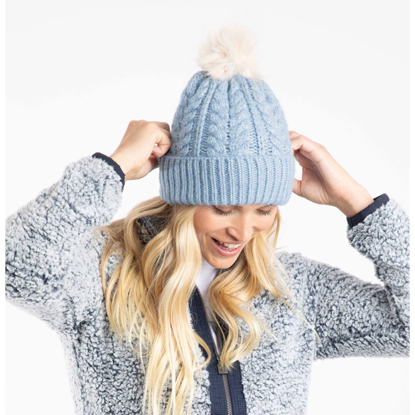 Woman wearing a Weird Fish light blue knit beanie with a pom-pom on a white background