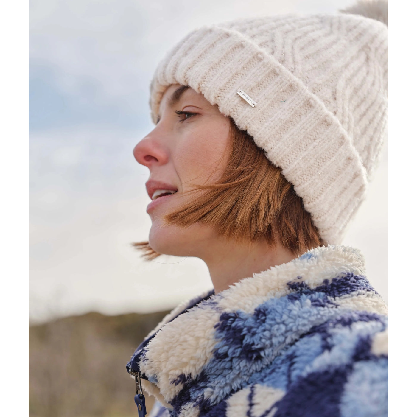 Woman wearing a chalk white knitted Blagdon beanie and patterned jacket outdoors
