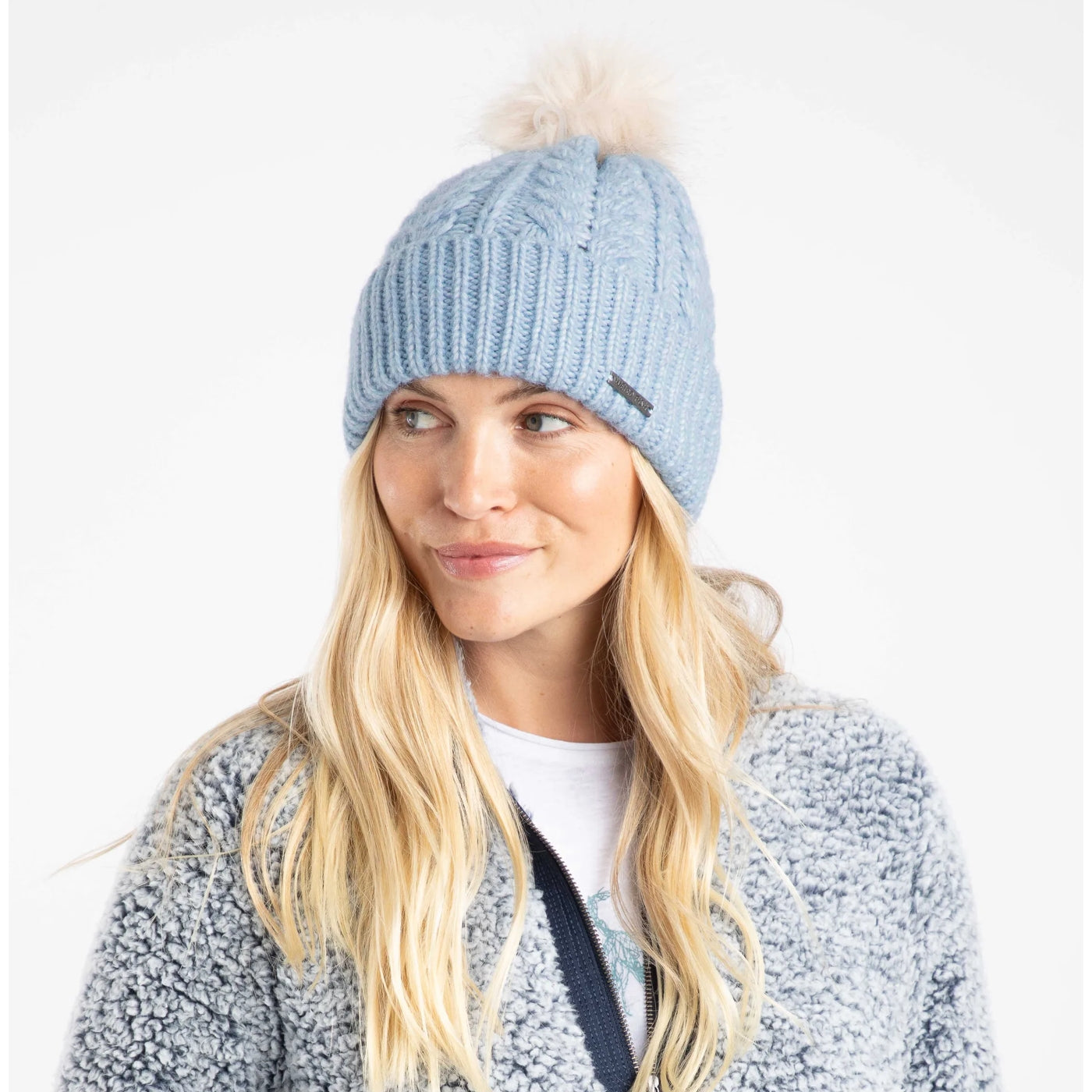 Woman wearing a light blue cable knit Weird Fish beanie with a pom-pom on a white background