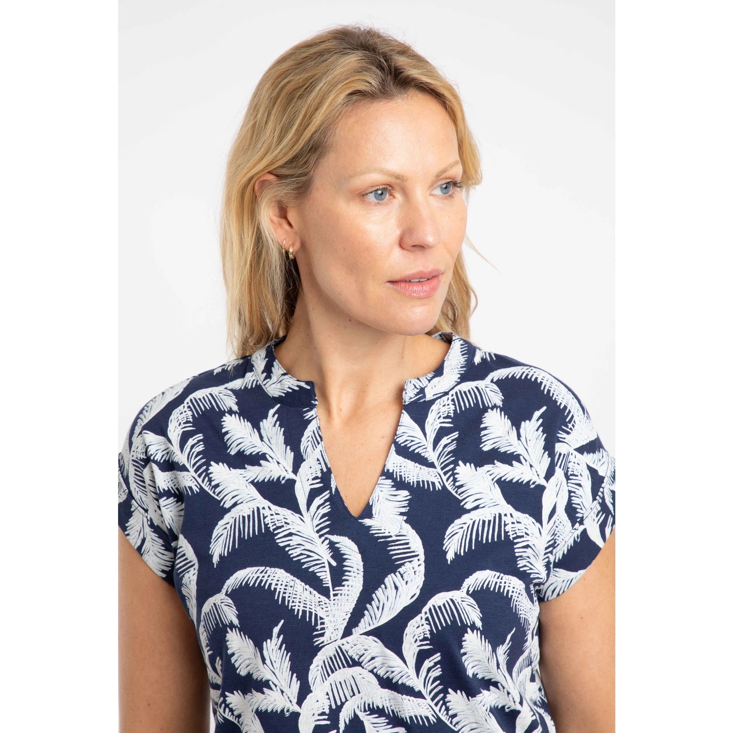 Close-up of a woman wearing an Ink blue Weird Fish Alia t-shirt with an ecru palm leaf pattern and notch neckline on a plain background
