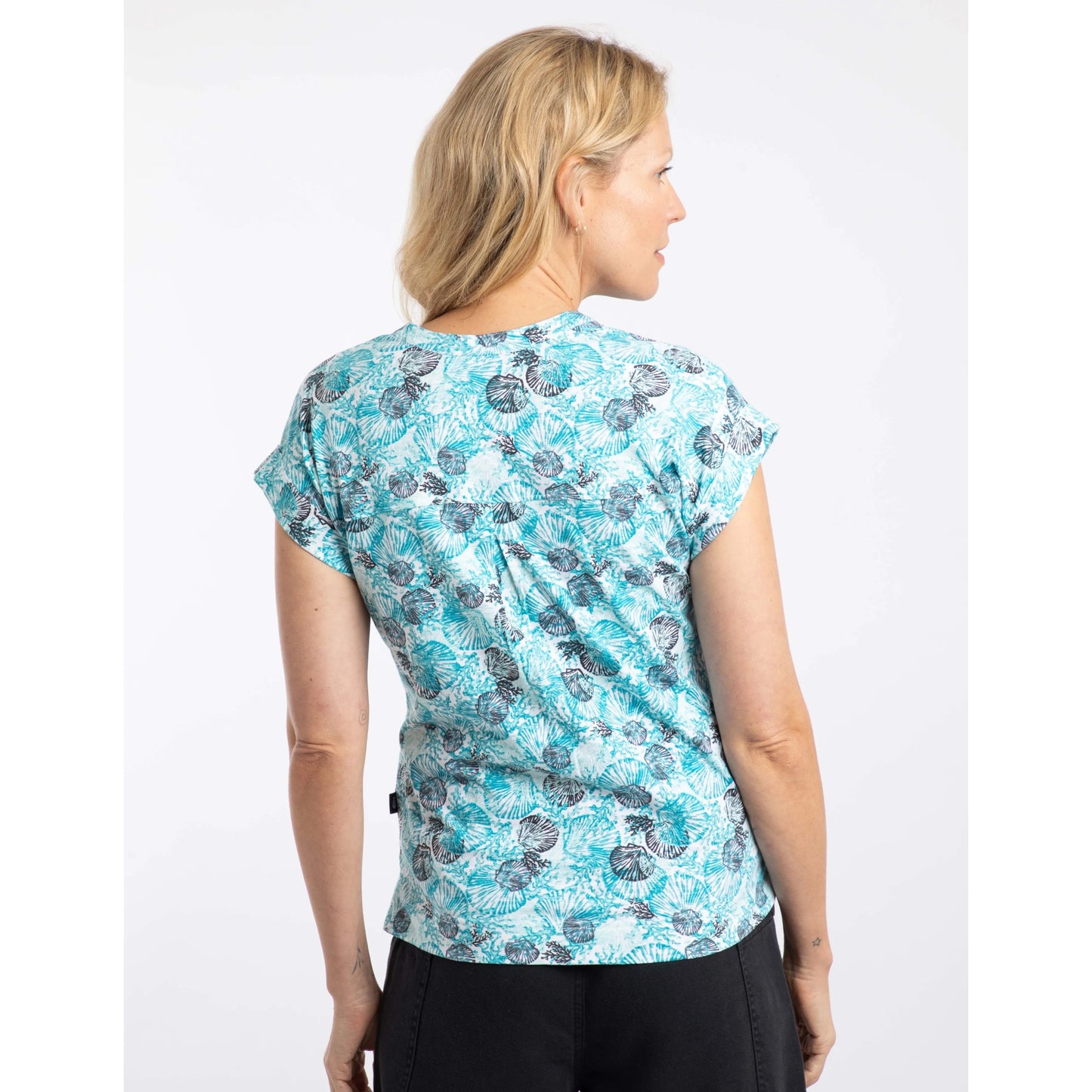 Back view of a woman wearing a Weird Fish short sleeve Alia t-shirt in an Ocean Blue shell pattern on a white background