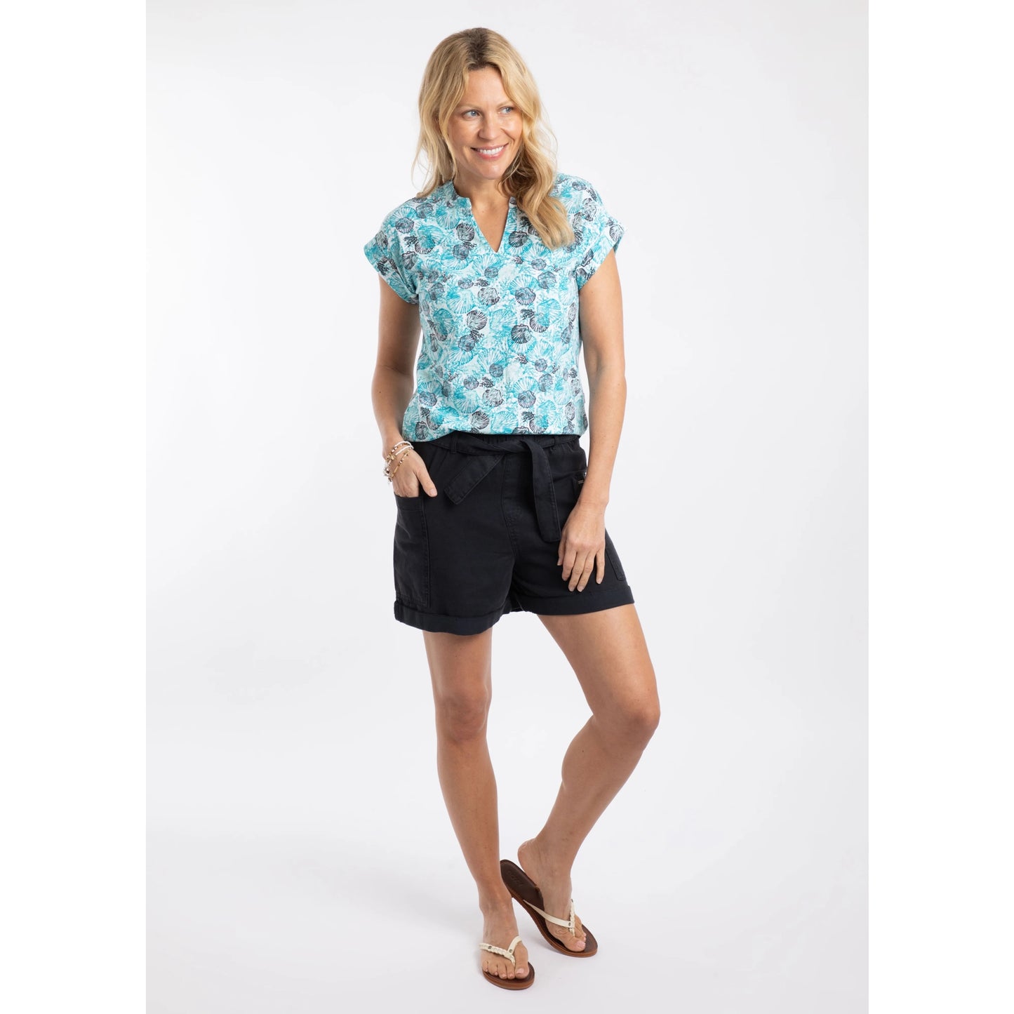 Woman wearing a Weird Fish shell patterned Alia t-shirt in Ocean Blue and black shorts on a white background