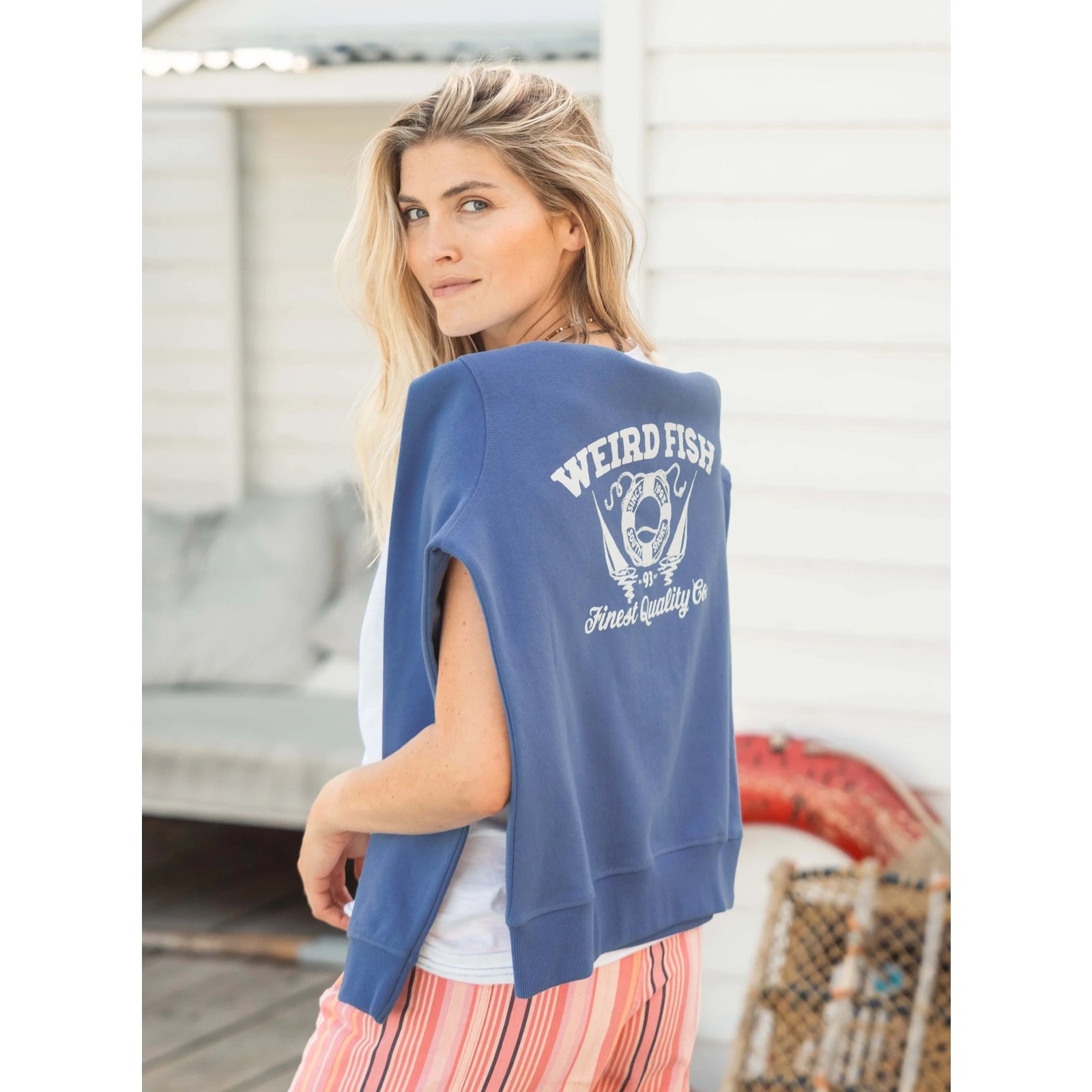 A woman with a Weird Fish Aurora crew neck sweatshirt in Faded Blue draped across the back of her shoulders.