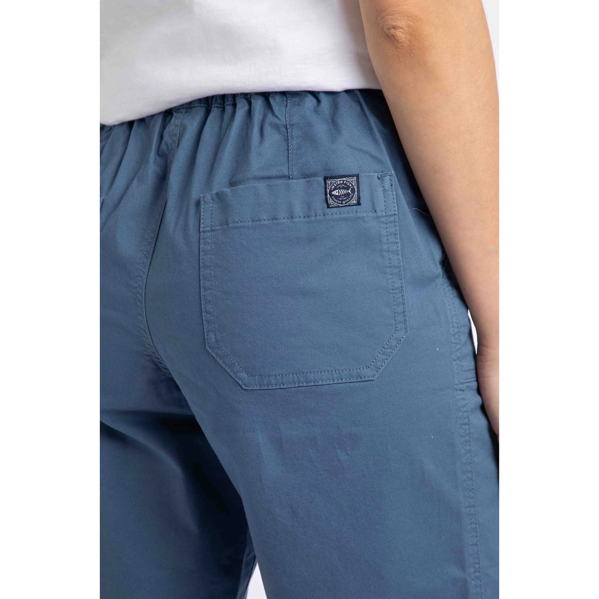Close-up view of the back pocket with logo label on a pair of womens Weird Fish flat front Kinnie shorts in Faded Blue with elastic waist and hip pockets.