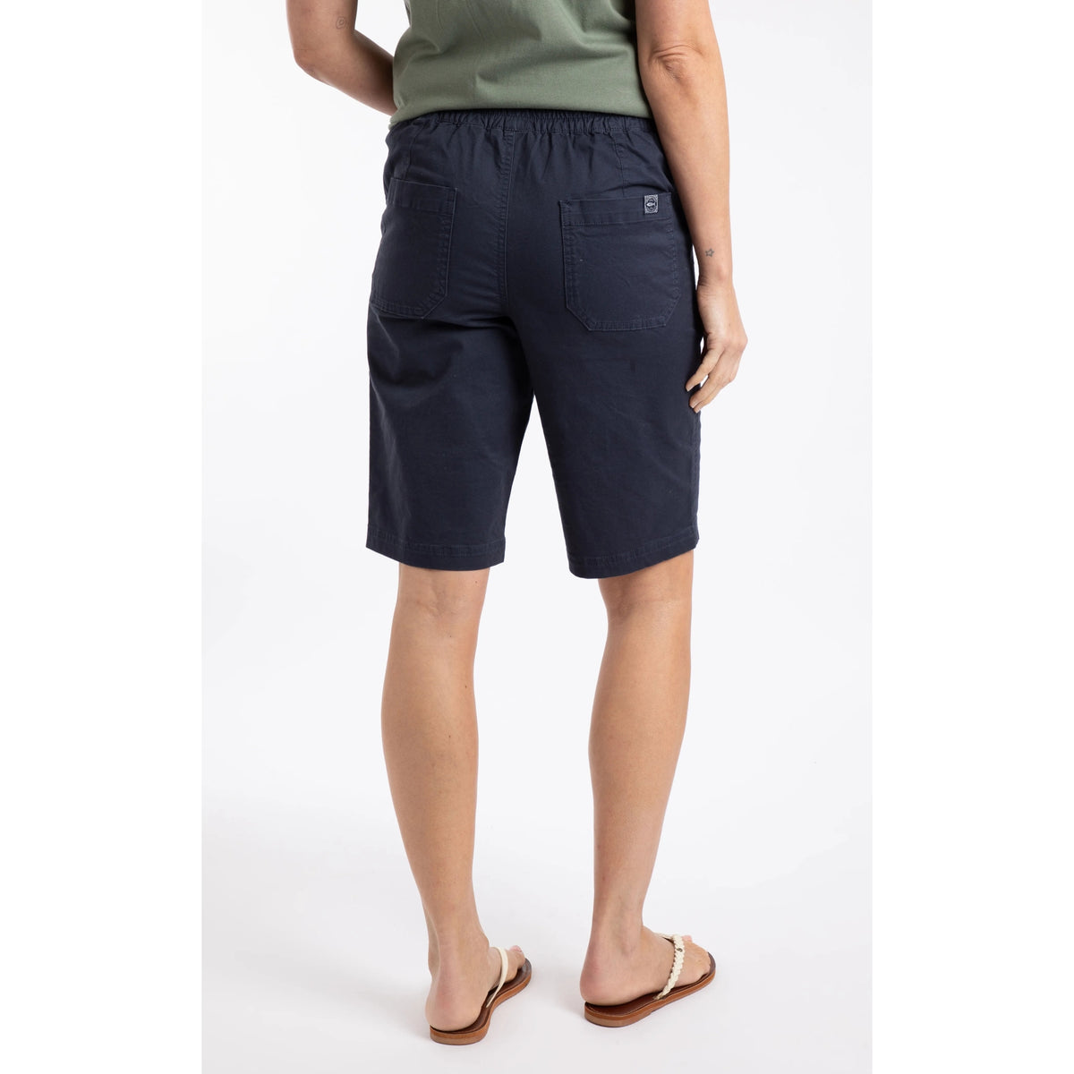 Back view of a woman wearing a pair of Weird Fish flat front Kinnie shorts in navy with elastic waist and hip pockets.