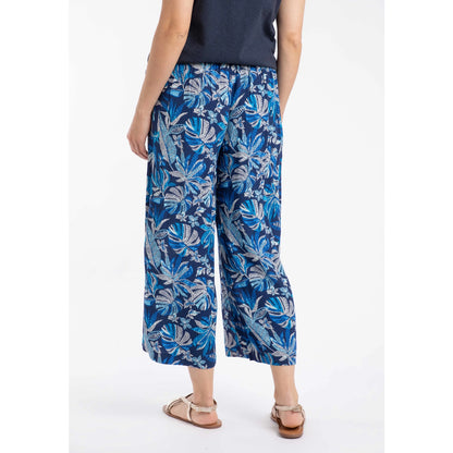 Back view of a woman wearing a pair of Weird Fish Sarita wide leg crinkle viscose cropped trousers in indigo blue with a tropical leaf pattern.