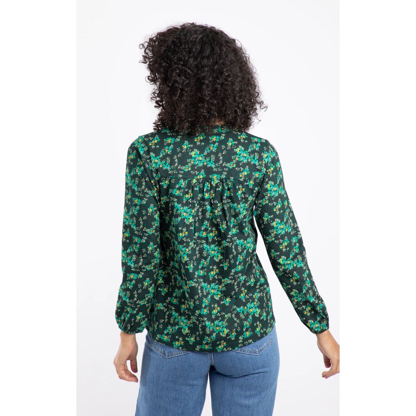 Back view of a woman wearing a green floral Weird Fish Brooke top with blue jeans on a white background