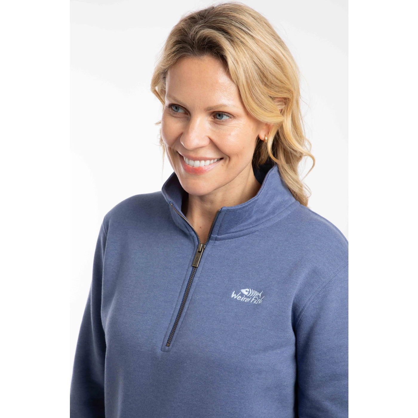 Close-up view of the 1/4 zip neckline and chest logo of a woman wearing a Weird Fish Avery sweatshirt in Faded Blue.