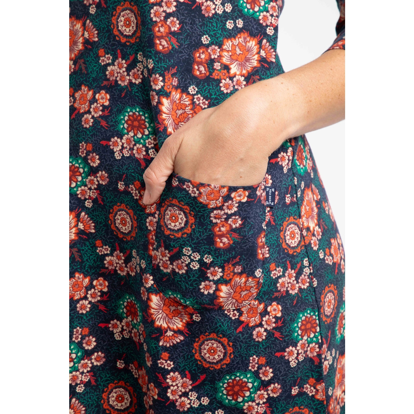 Close-up of a Weird Fish blue, coral and red floral patterned dress with a hand in the pocket.