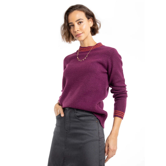 Woman wearing a Weird Fish Beet purple Dawkins knitted jumper and a grey skirt on a white background