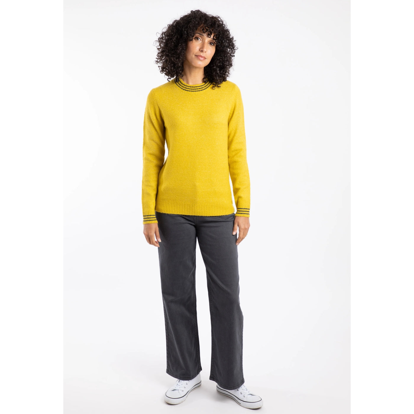 Woman wearing a Weird Fish yellow Dawkins jumper and grey trousers on a white background