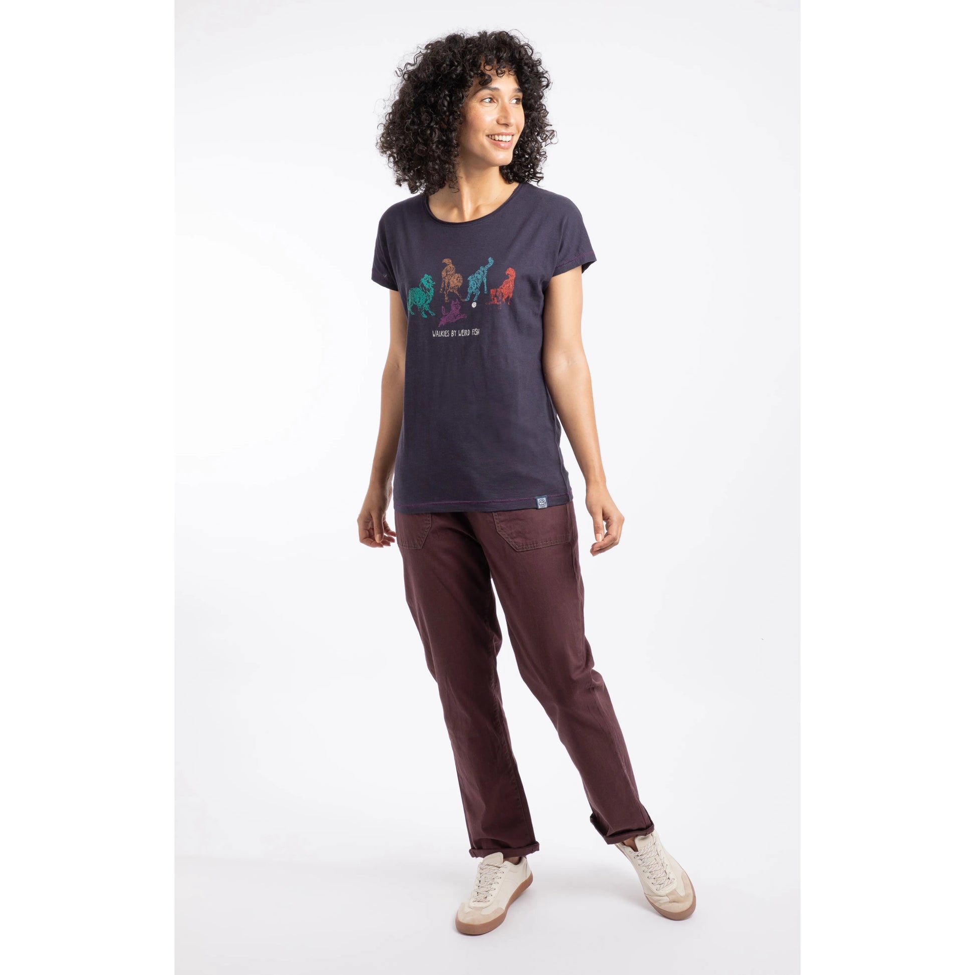 Woman wearing a navy t-shirt with a colourful dog graphic and brown pants on a white background