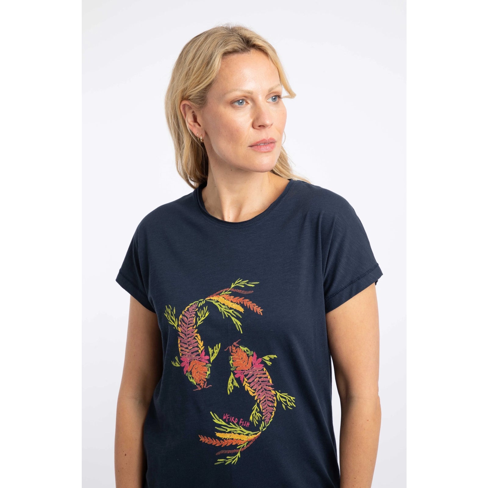 Close-up view of a woman wearing a Weird Fish short sleeve navy t-shirt featuring an abstract koi carp print made up of fern leaves on the front.