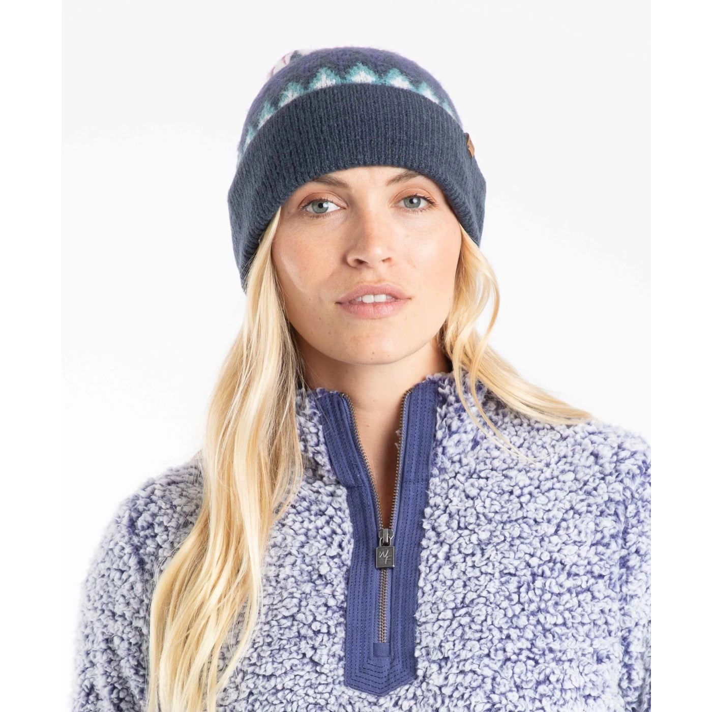 Woman wearing a navy blue knitted Weird Fish Frady beanie and a fleece jumper with a zip on a white background