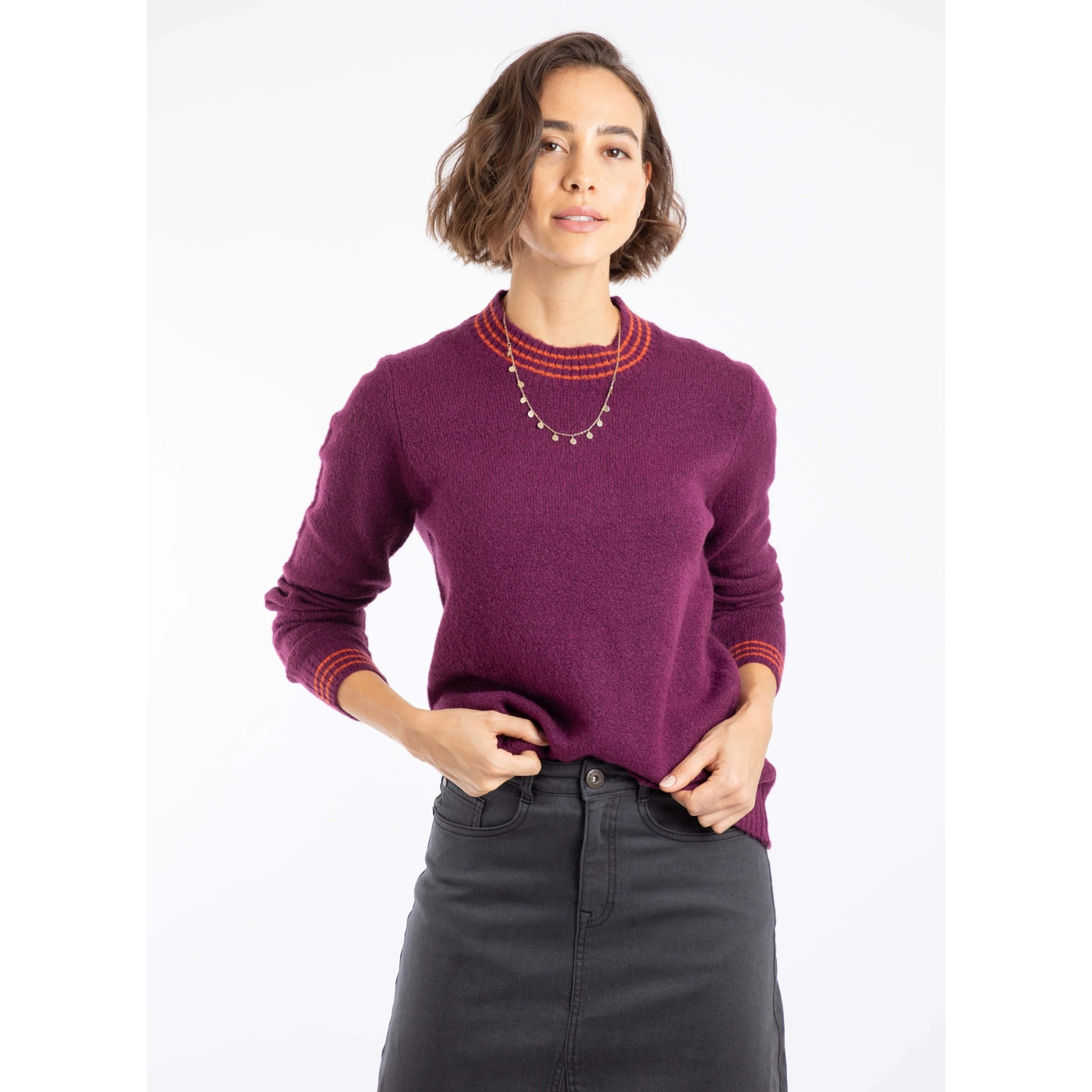 Woman wearing a Weird Fish Dawkins beet purple knitted jumper with red trim on a white background