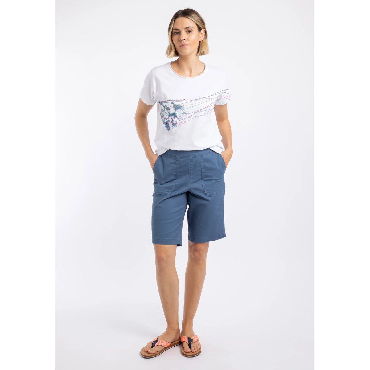 A woman wearing a pair of Weird Fish flat front Kinnie shorts in Faded Blue with elastic waist and hip pockets, twinned with a white t-shirt.