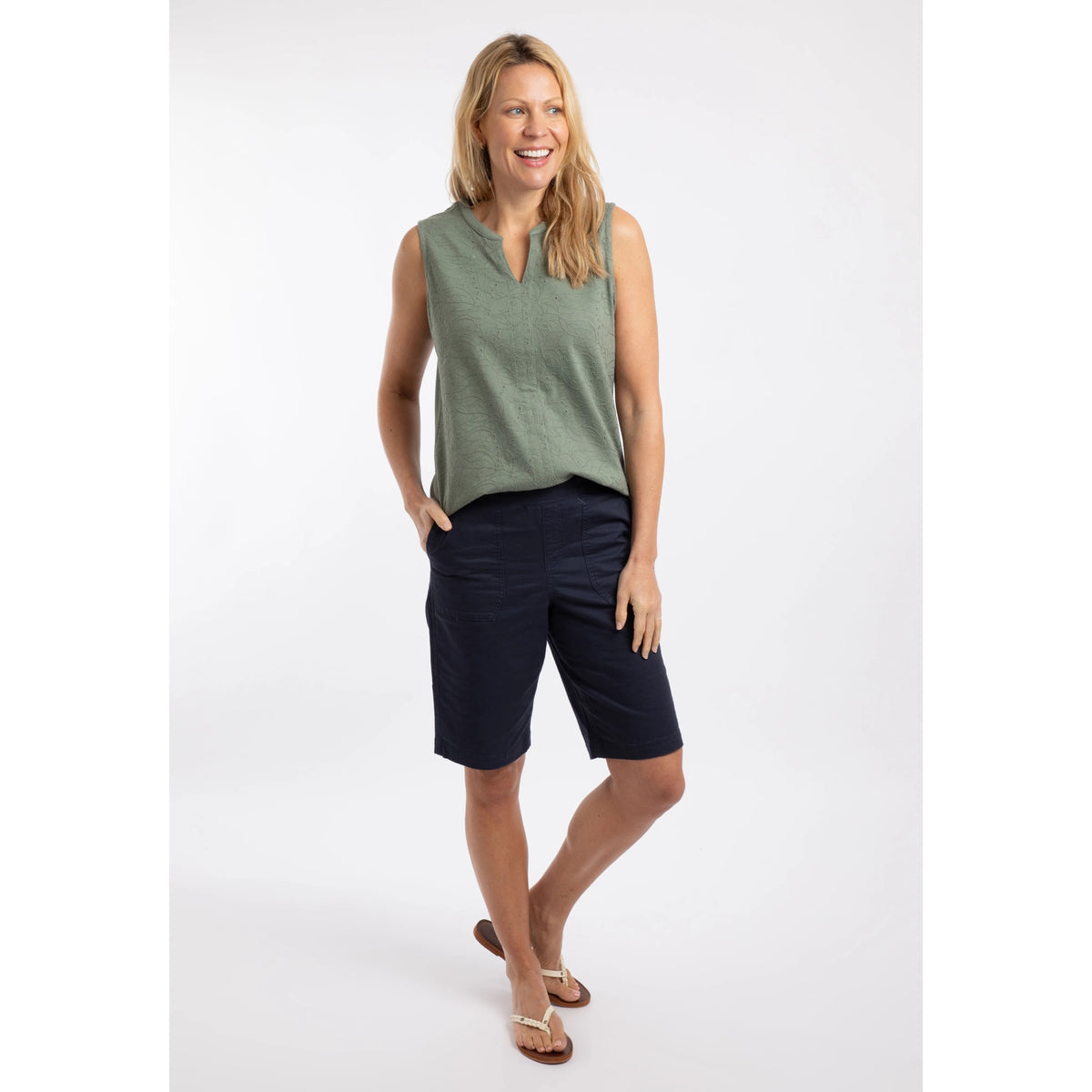 Woman wearing a pair of womens Weird Fish flat front Kinnie shorts in navy with elastic waist and hip pockets, twinned with a green vest.