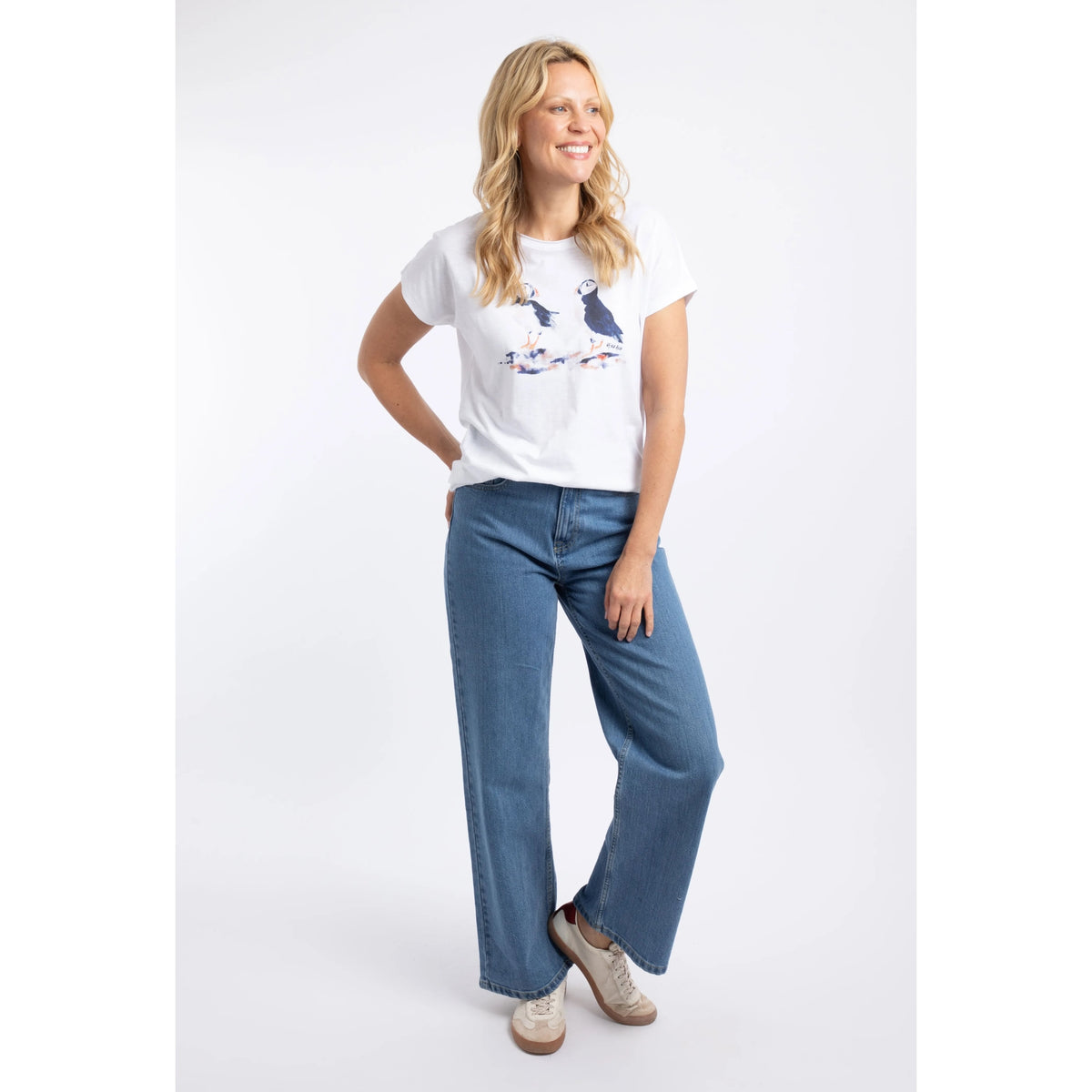 A woman wearing a Weird Fish white Puffin print t-shirt with blue jeans.