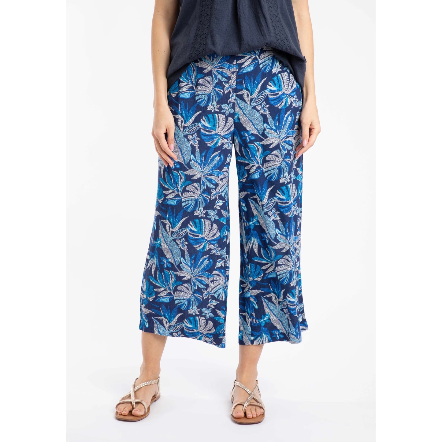 Front view of a woman wearing a pair of Weird Fish Sarita wide leg crinkle viscose cropped trousers in indigo blue with a tropical leaf pattern.