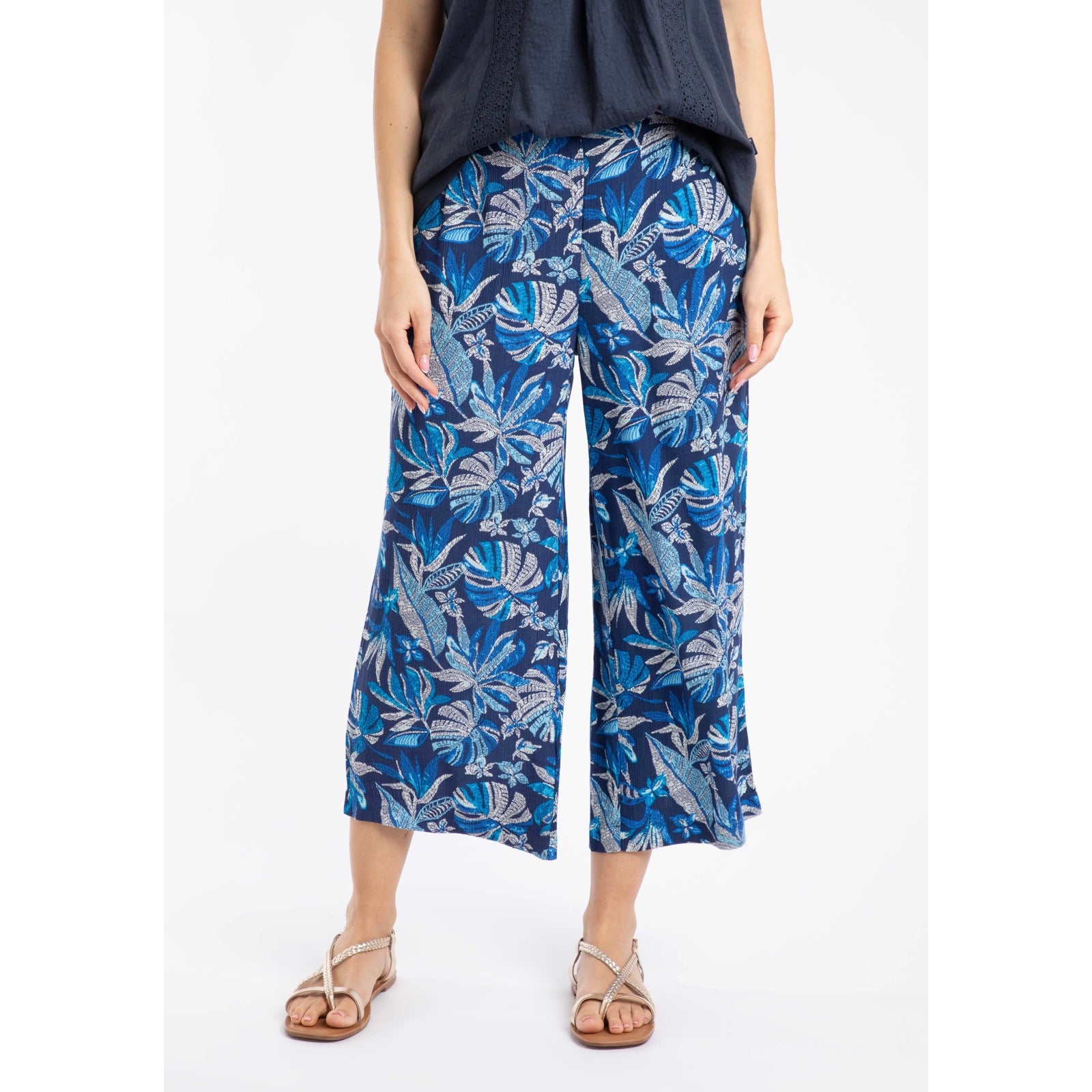 Front view of a woman wearing a pair of Weird Fish Sarita wide leg crinkle viscose cropped trousers in indigo blue with a tropical leaf pattern.