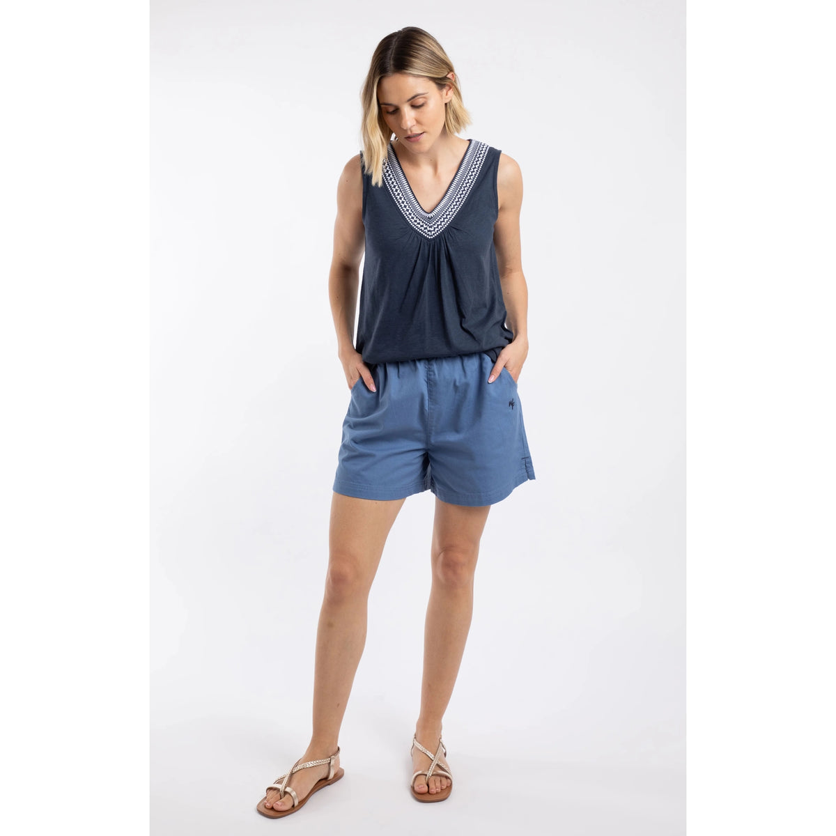 A woman wearing a pair of Weird Fish Jardin elastic waist twill cotton shorts in Faded Blue with hip pockets and small embroidered logo, paired with a navy vest.