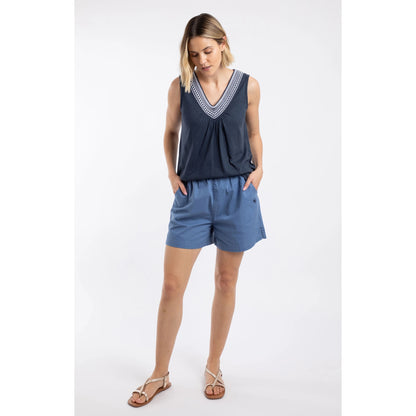 A woman wearing a pair of Weird Fish Jardin elastic waist twill cotton shorts in Faded Blue with hip pockets and small embroidered logo, paired with a navy vest.