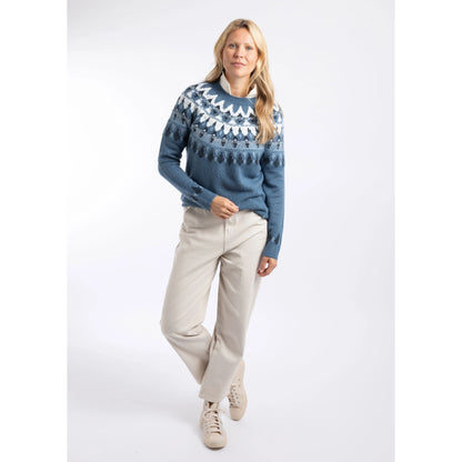 A woman wearing a Weird Fish knitted Lowell jumper in Ash Blue, with a Fair Isle pattern across the chest and shoulders with trousers and trainers.