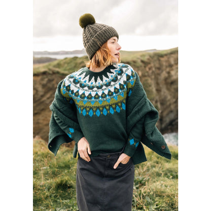 Front view of a woman wearing a Weird Fish knitted Lowell jumper in Bottle Green, with a Fair Isle pattern across the chest and shoulders, stood outdoors wearing a bobble hat and jacket.