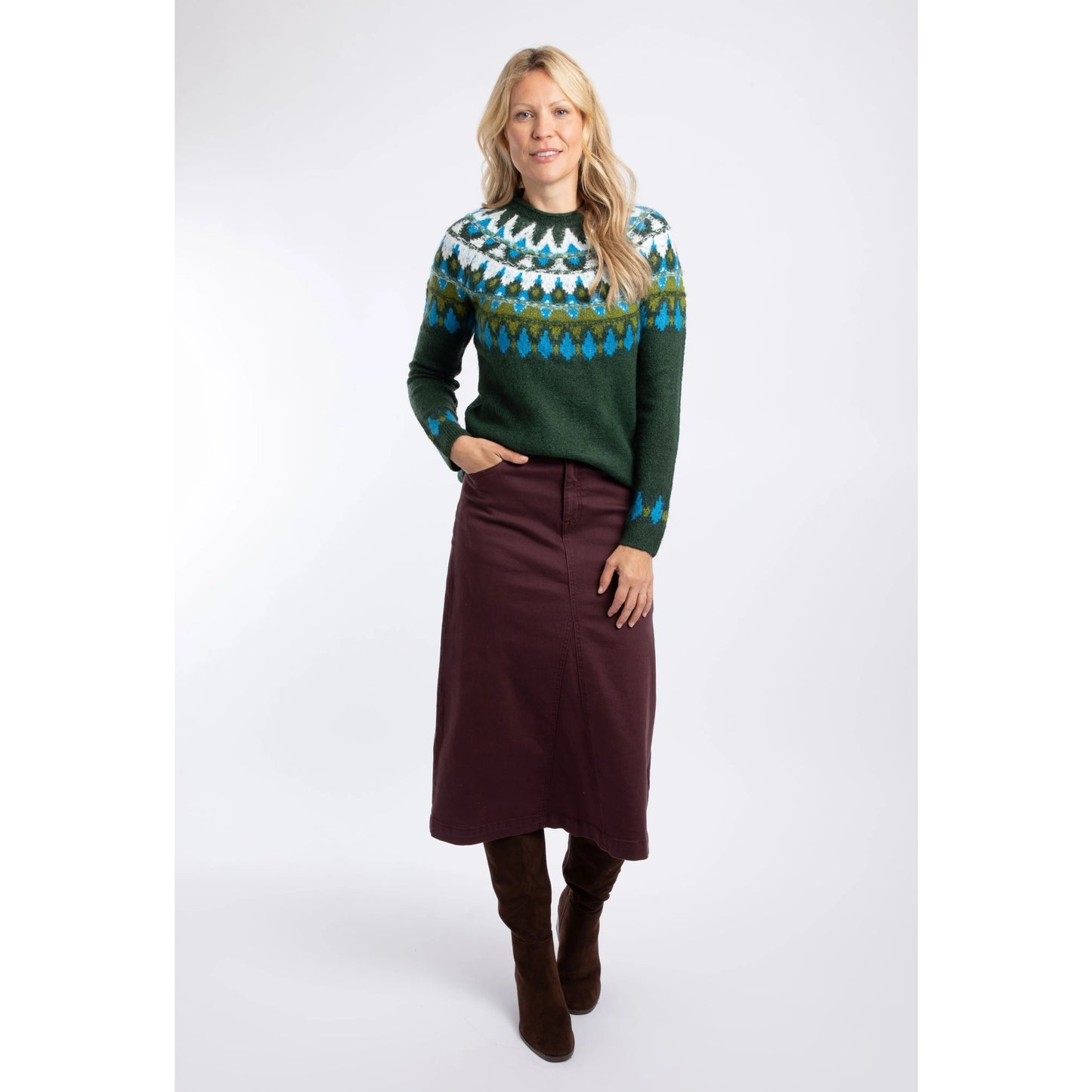 A woman wearing a Weird Fish knitted Lowell jumper in Bottle Green, with a Fair Isle pattern across the chest and shoulders with as skirt and boots.