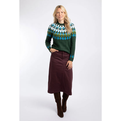 A woman wearing a Weird Fish knitted Lowell jumper in Bottle Green, with a Fair Isle pattern across the chest and shoulders with as skirt and boots.
