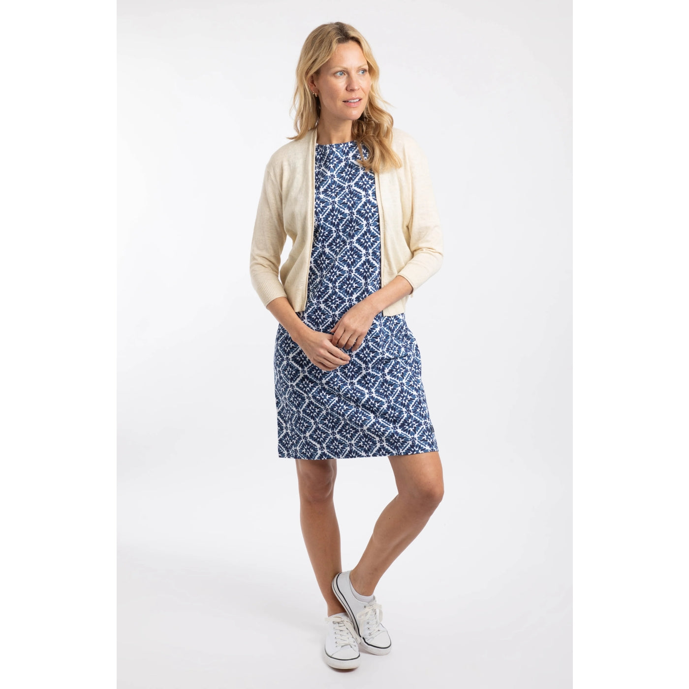 Woman wearing a Weird Fish Limon 3/4 sleeve shrug cardigan in Light Cream of a blue tile pattern dress