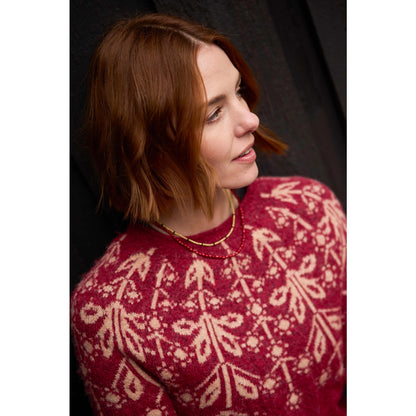 Closeup of a woman wearing a red Weird Fish Miska knitted jumper with a Fair Isle pattern on a dark brown background