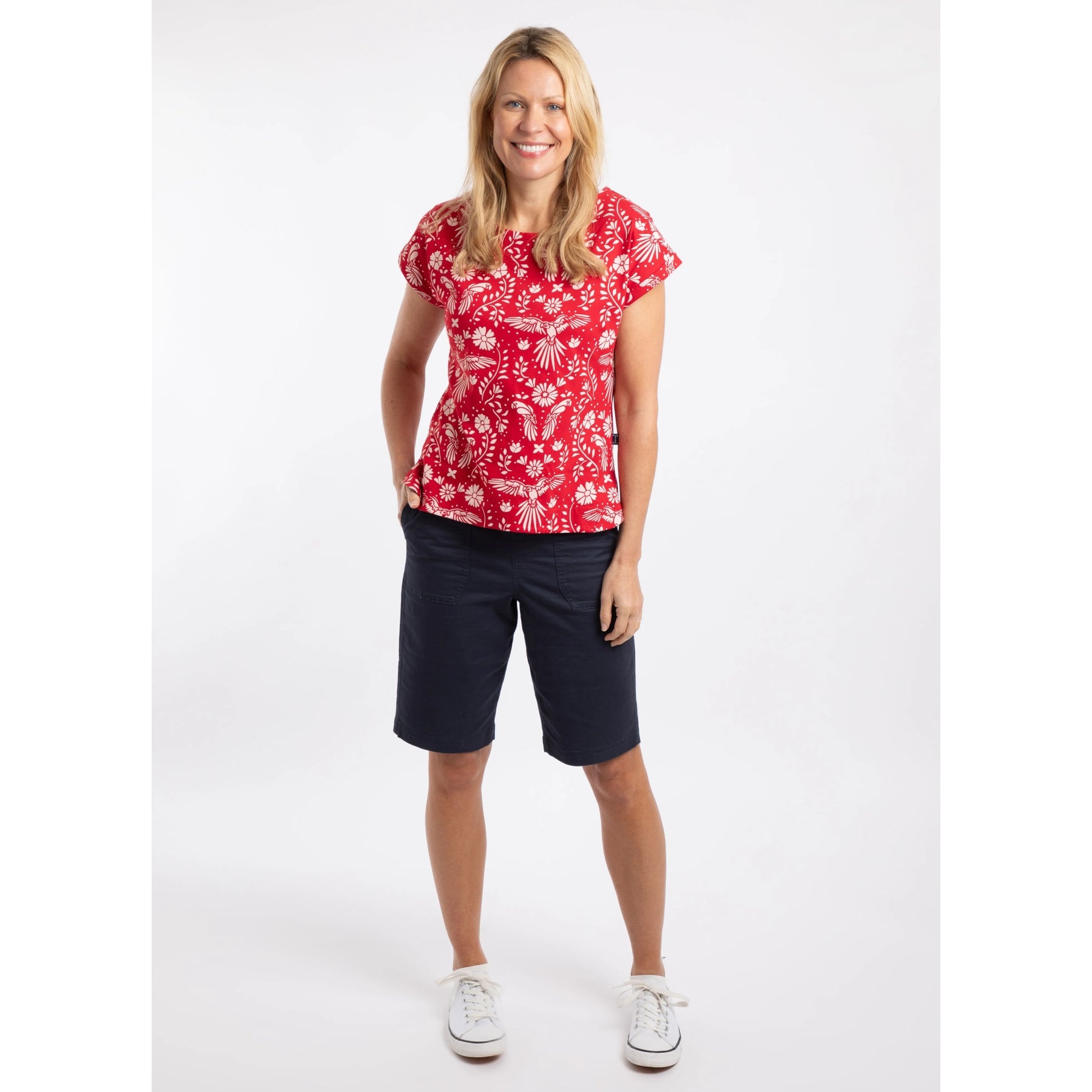 Woman wearing a Rich Red short sleeve Weird Fish Paw Paw t-shirt with a white floral pattern with navy shorts on a white background