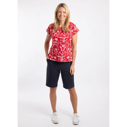 Woman wearing a Rich Red short sleeve Weird Fish Paw Paw t-shirt with a white floral pattern with navy shorts on a white background