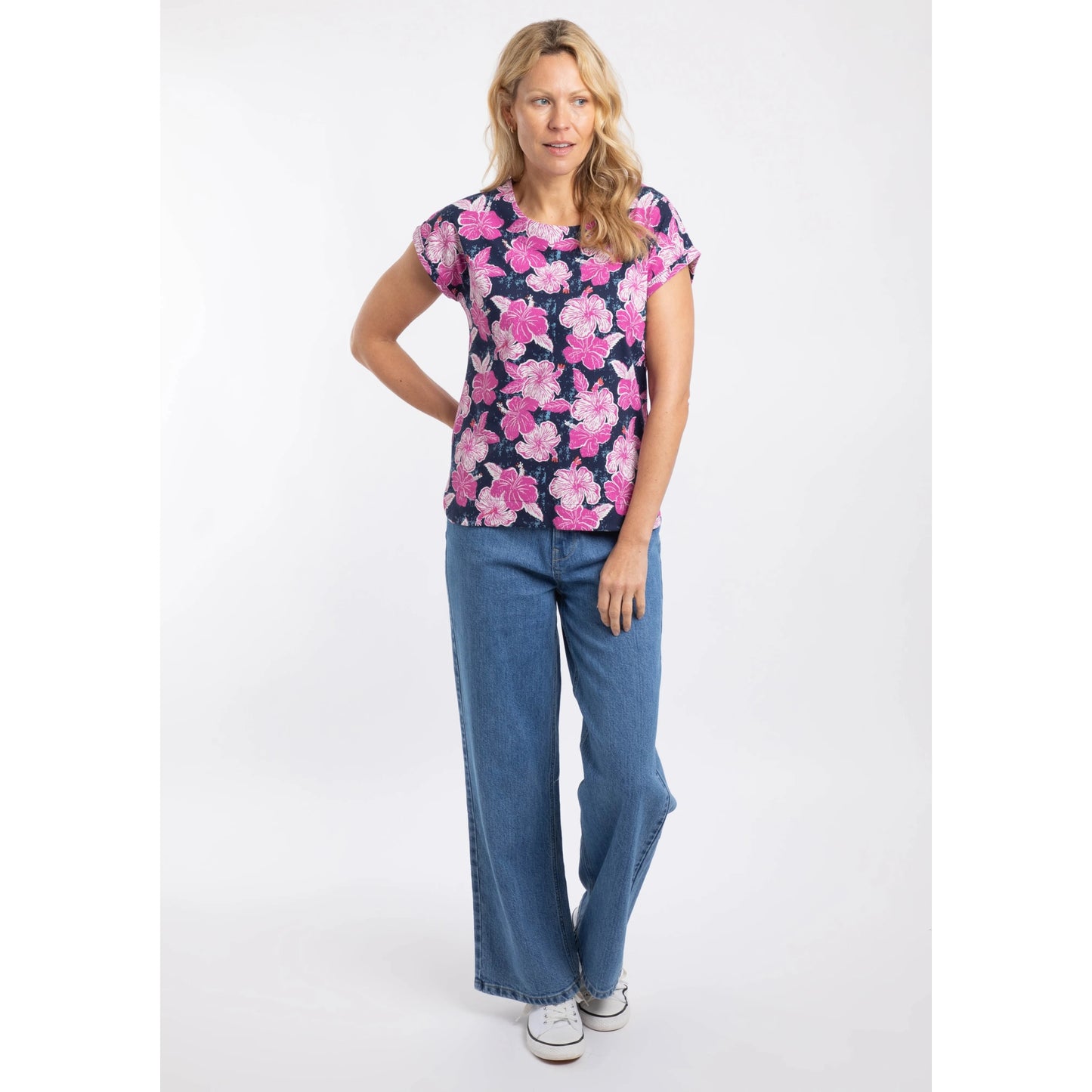 A woman wearing a Weird Fish Paw Paw t-shirt with a pink floral pattern with jeans on a white background