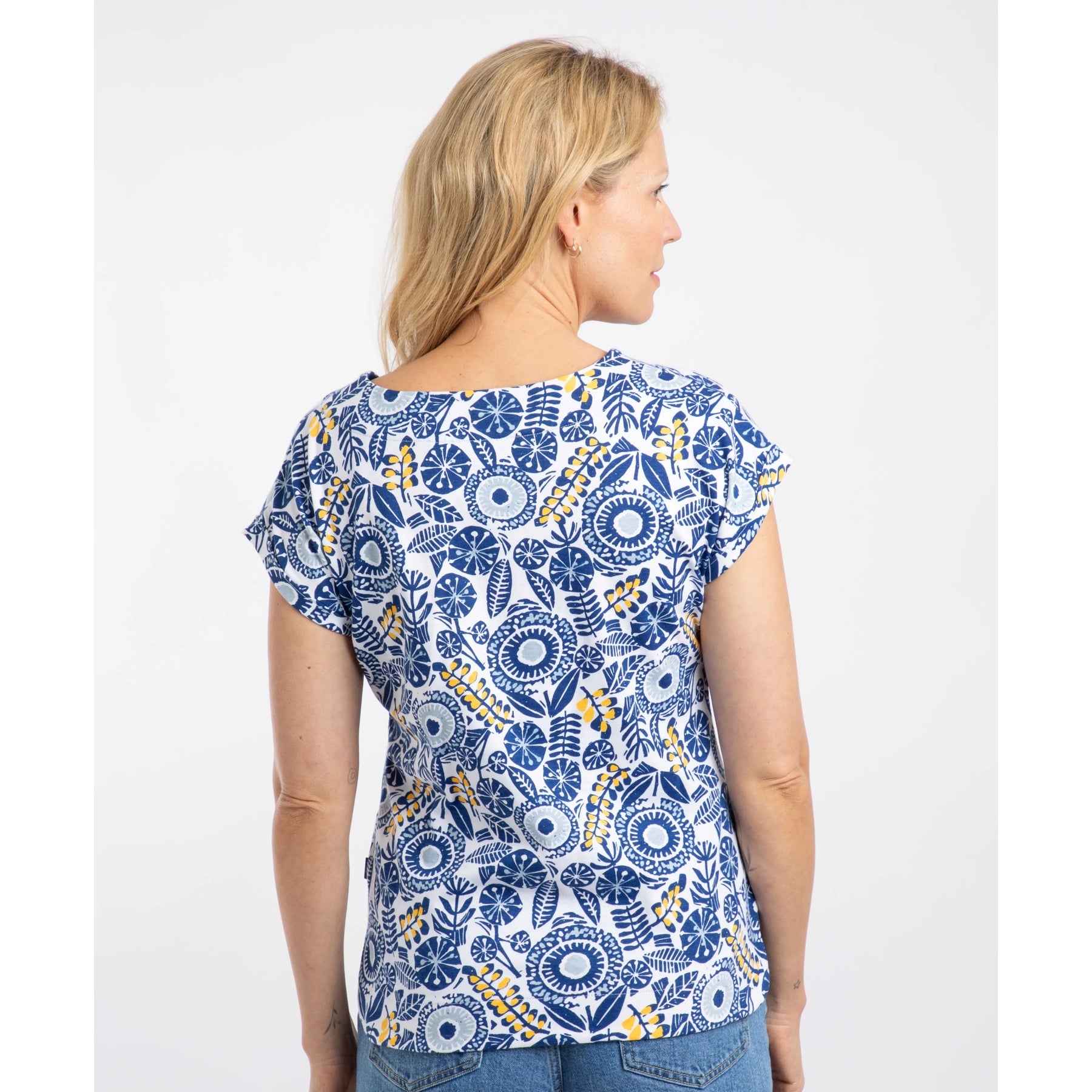 Back view of a woman wearing a Weird Fish blue floral patterned Paw Paw t-shirt on a white background
